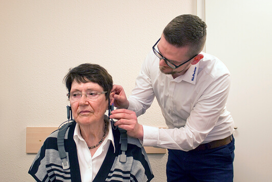 Ein Hörakustiker passt einer Seniorin ein Hörgerät zur Hörtest-Diagnose im Fachgeschäft an.