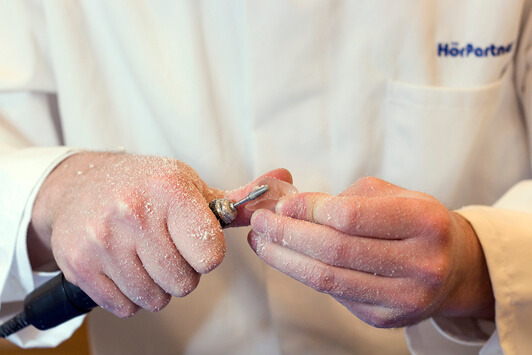 Ein Hörakustiker bearbeitet ein Hörgerät mit einem Fräswerkzeug in der Werkstatt.